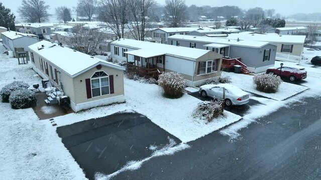 Mobile home with snow falling in USA. Low income houses. Manufactured housing. Aerial during snow storm in winter.