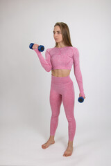 A fitness trainer in a pink training suit shows warm-up exercises with dumbbells.