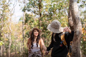 Fototapeta premium Cheerful romantic lesbian couple traveler with backpack on their backs go hiking through the forest in the mountains in summer