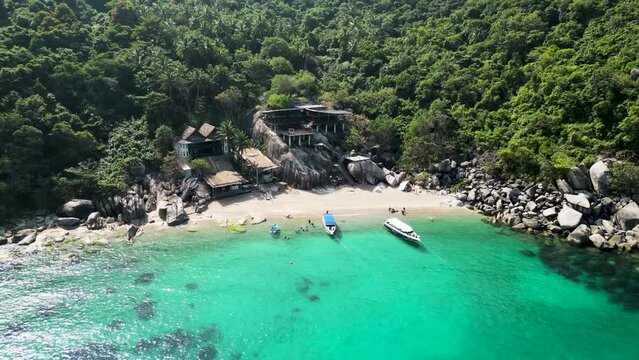 Boats on an inlet with cabins in Mango Bay Ko Tao Island Thailand with tourists at beach, Aerial descent tilt up shot
