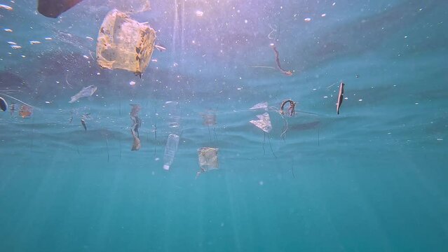 Floating plastic debris on the water’s surface, with one piece prominently in the foreground, showcasing ocean pollution. Check the gallery for similar footages.