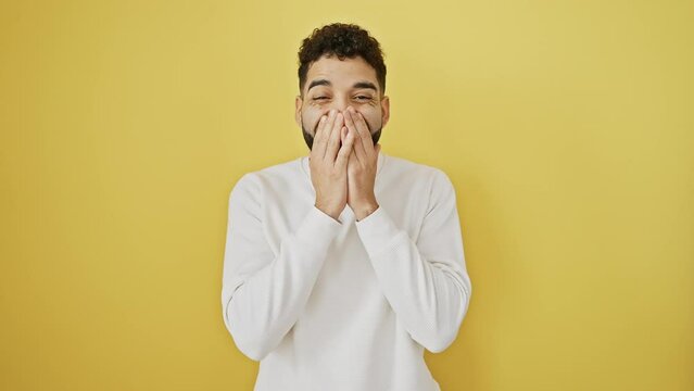 Laughing young man covering mouth with hand, embarrassed by juicy gossip, scandal brewing against an isolated yellow background