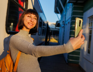 Fototapeta premium beautiful tourist takes a selfie at the station near the train. Girl with a backpack at the station.