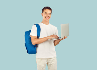 Happy clever tech high school coder student boy standing on light background uses laptop computer,...