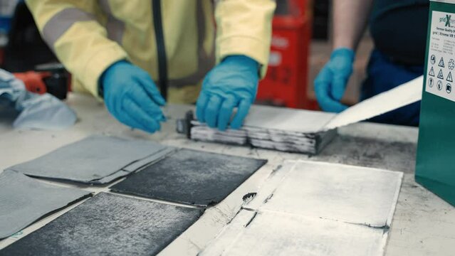 Close up how carbon and seperator layers of a big battery get layed down across the table by two workers in terms of quality control an condition check