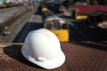A white safety helmet is placed on rustic platform floor with background of the freight train locomotive that stop at the logistic factory. Industrial safety equipment object.