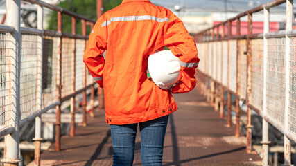 An engineer or construction worker is holding a white safety helmet, wearing orange coverall,...