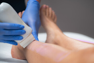 Obraz na płótnie Canvas Skilled beautician removes unwanted hair from a female leg using wax strips, unveiling a smooth and flawless result
