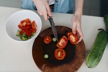 Fresh and Healthy Tomato Salad: A Woman's Hands Cutting Fresh Green Vegetables on a Wooden Chopping Board with a Red Tomato.