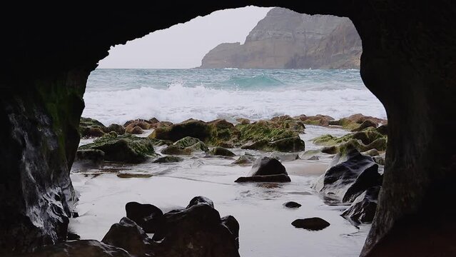 Amazing Closeup of Natural Rock Arch window on beach coast with fog, sand, moss, pebbles and waves, Porto Santo island, Madeira, 50fps HD.