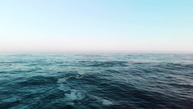 Drone flying low across open waters at sea, panning 180 degrees showing the town Vermont with houses on the beach front overlooking the ocean with boulders on the beach on a misty morning