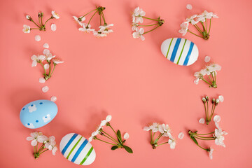 White flowers, cherry blossoms and Easter eggs with blue stripes on a pink background. Easter background, copy space. Flatlay