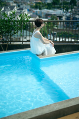 プールサイドでくつろぐ白いワンピースを着たショートヘアの女性