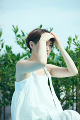 緑のある庭に佇む白いワンピースを着たショートヘアの女性