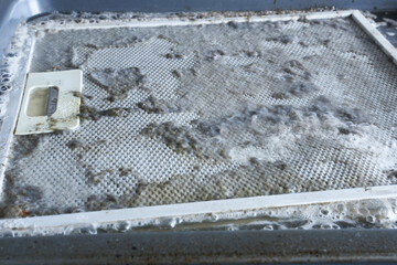 Cleaning the hood filter. Dirty kitchen hood filter in cleaning solution, closeup photo.