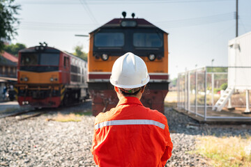 Back from a female engineer in safety working uniform, wearing peotective helmet is standing in front of the train locomotive head. Ready to working in challenge logistic industrial concept.