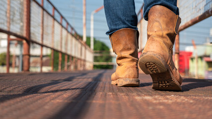 Close-up at worker feet is wearing leather safety boots during walking on rustic walkway platform....