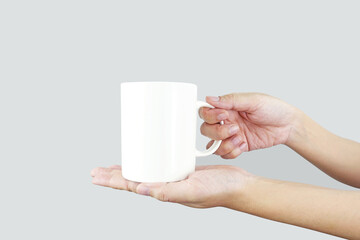 Hands holding a mockup of a white empty mug on a gray background,  for your logo design. with clipping path.