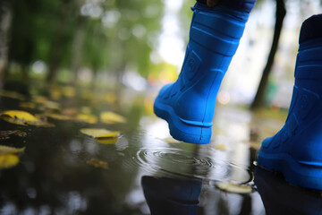 legs of child in blue rubber boots jumping in the autumn puddles