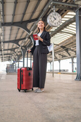 Young asian business woman holding phone and passport at a train station, waiting to departure to the city center