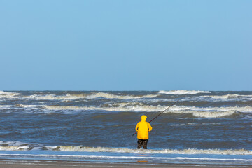 A fisherman seen from behind standing in the rough sea of the North sea close to the beach