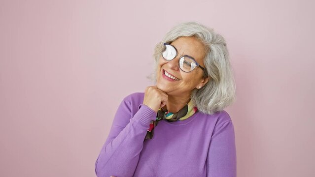 Thinking grey-haired woman, pensive expression filled with doubt over pink background