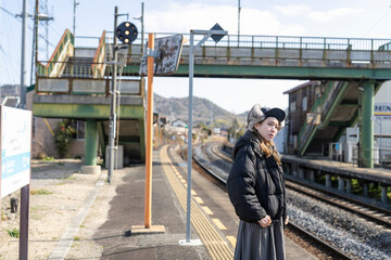 田舎の駅のホームで電車を待つ女性