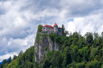 Castle on top of rock with waving Slovenian flag at lakeshore of Slovenian Lake Bled on a blue cloudy summer day. Photo taken August 8th, 2023, Bled, Slovenia.