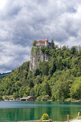 Fototapeta na wymiar Scenic view of castle on top of rock with Slovenian flag waving at lakeshore of Slovenian Lake Bled on a cloudy summer day. Photo taken August 8th, 2023, Bled, Slovenia.