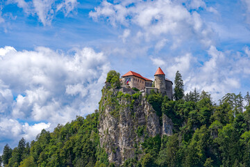 Scenic view of castle on top of rock with Slovenian flag waving at lakeshore of Slovenian Lake Bled...