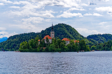 Fototapeta na wymiar Lake Bled with church on an island and woodland in the background on a cloudy summer day. Photo taken August 8th, 2023, Bled, Slovenia.
