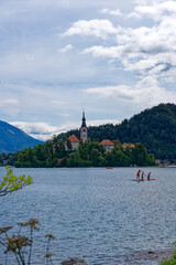 Obraz premium Lake Bled with church on an island and woodland in the background on a cloudy summer day. Photo taken August 8th, 2023, Bled, Slovenia.