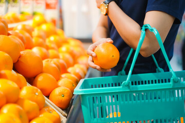 Woman holding grocery basket walk in supermarket. Attractive. female hold orange fruit pick up from...