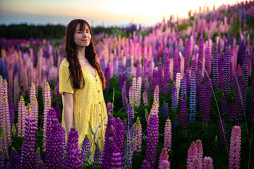 beautiful girl in yellow dress enjoying a walk in the field of lupins on sunset; colorful flowers...