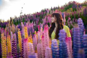 beautiful girl in yellow dress enjoying a walk in the field of lupins on sunset; colorful flowers...