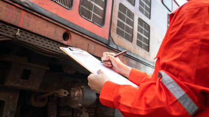 A technician is checking on heavy machine maintenance checklist, with train locomotive engine cabin part as blurred background. Transportation industrial working scene, selective focus at hand. - obrazy, fototapety, plakaty