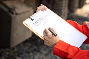 	
Action of a mechanic engineer is checking on heavy machine checklist form to verify the quality of maintenance service, with train locomotive part as blurred background. Industrial working scene.