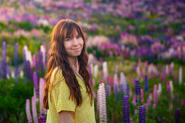 beautiful girl in yellow dress enjoying a walk in the field of lupins on sunset; colorful flowers...