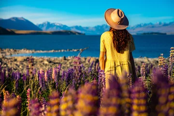 Fototapete Aoraki/Mount Cook beautiful girl in yellow dress and hat standing on the field of colorful lupins and enjoying the sunset over lake tekapo  unique flowers near mountaineous lake in new zealand, south island, canterbury
