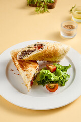 Grilled beef shawarma sandwich on a white plate, garnished with fresh lettuce and tomato. Suitable for fast food advertising and snack bar menus