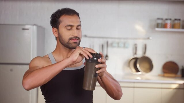 Happy Middle aged fit man drinking protein shake from bottle at kitchen after morning workout - concept of muscle supplement and stamina or body building