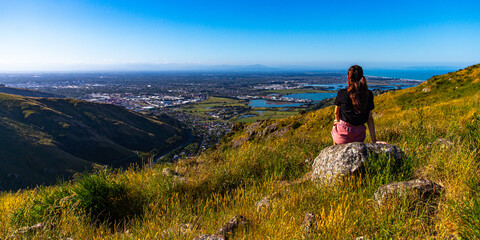 Obraz premium pretty girl sitting at the top of hill and watching the panorama of christchurch; hiking bridle path in christchurch