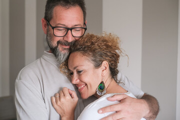 Beautiful middle-aged Caucasian couple hugging each other tenderly, exchanging cuddles and...