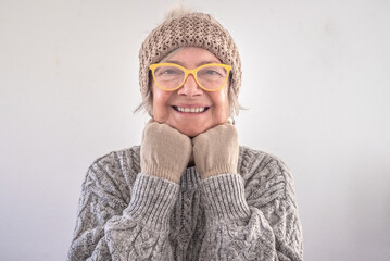 Portrait of smiling senior woman in gray sweater with glasses and cap looking at camera, isolated...