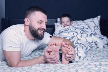 Bare feet of a child. Dad tickles his child's feet sticking out from under the blanket. Laughter...