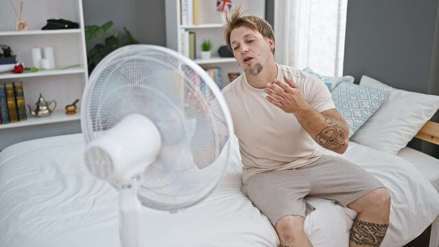 Blond man feeling hot summer bedroom cooling wind fan