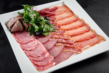Assorted deli meats on a white square plate on a textured black background