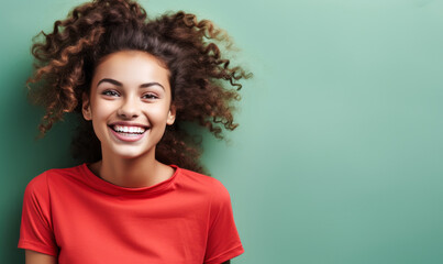 Delightful young girl with a captivating smile and playful curly hair in a bright red shirt against a soft mint green background