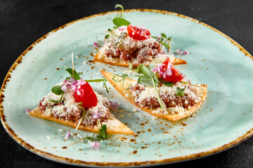 Elegant beef tartare on crispy toasts with parmesan, greens, and tomatoes on a speckled turquoise plate