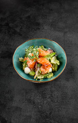 Salad with salmon, mozzarella, and avocado, served in a turquoise ceramic bowl
